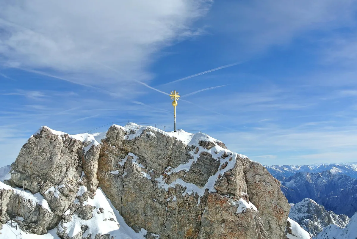 Goldenes Gipfelkreuz auf der Zugspitze zwischen Schnee und Fels in Garmisch-Partenkirchen
