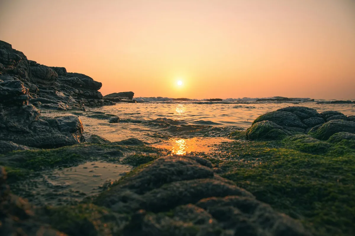 Pôr do sol sereno sobre costa rochosa coberta de musgo com ondas suaves do oceano