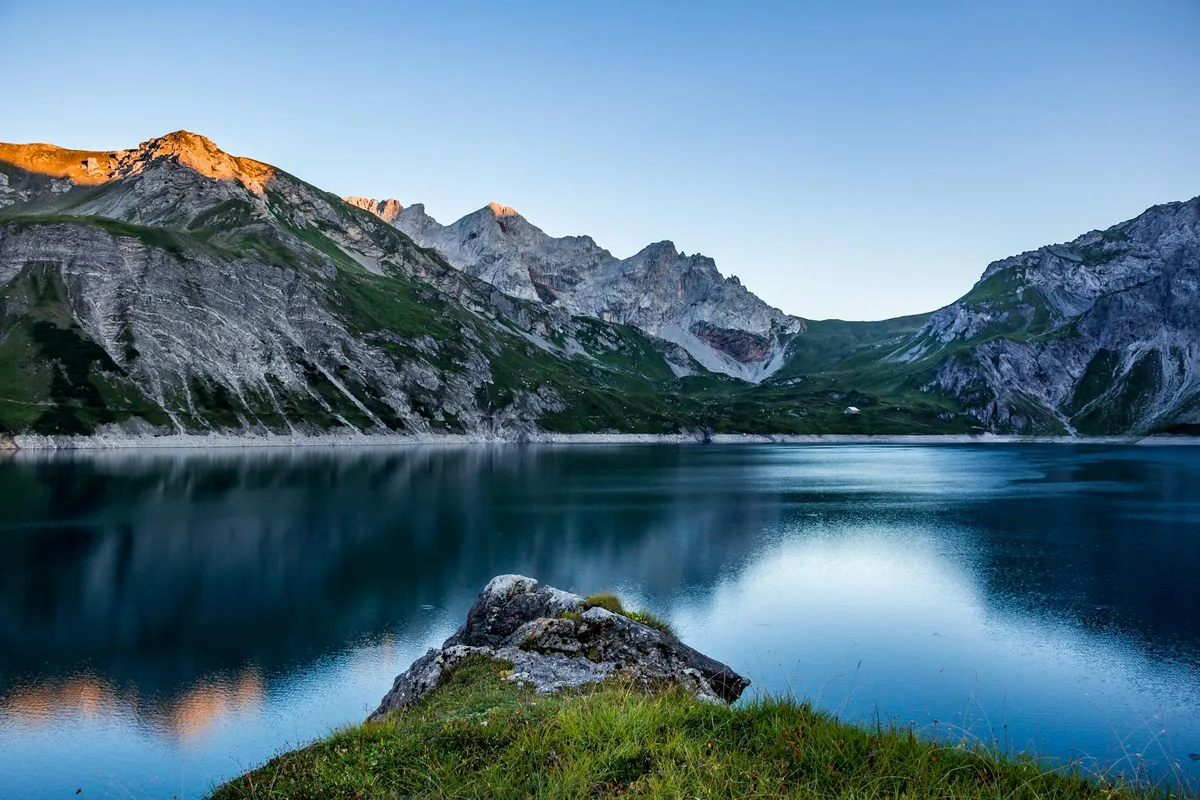 Österreichischer Alpensee mit majestätischen Bergen und Grün bei Sonnenaufgang