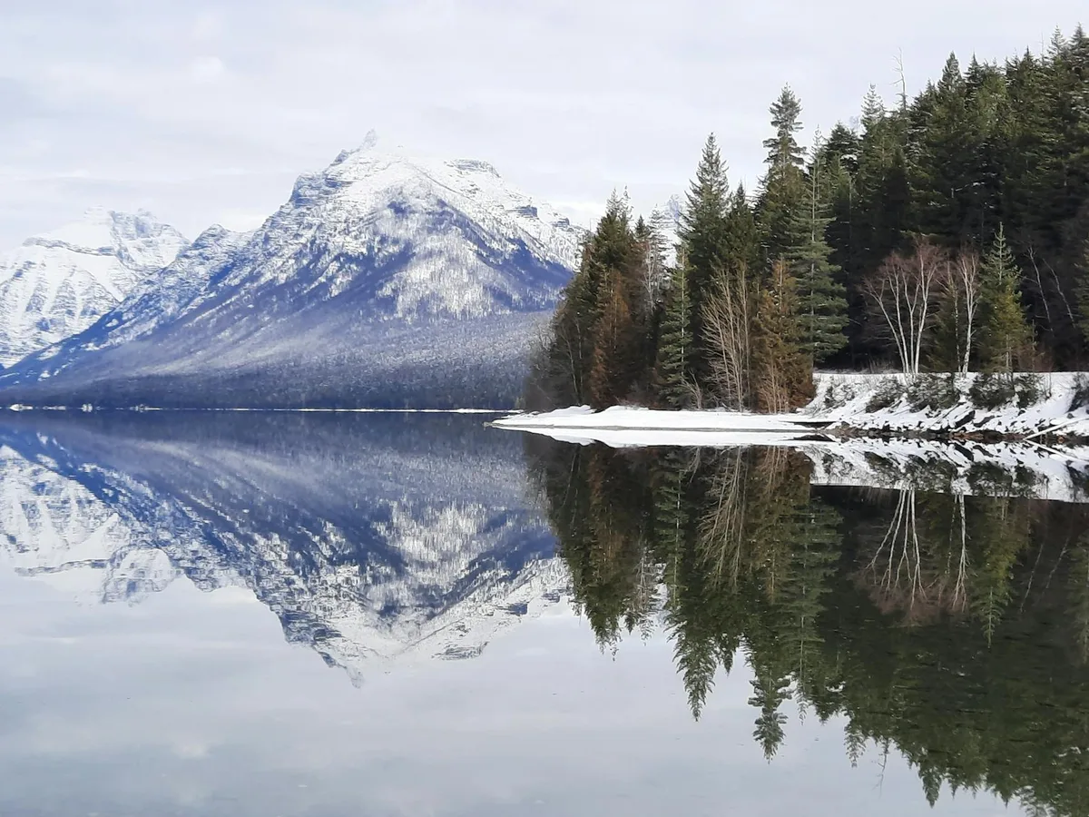 Paisagem serena de montanhas nevadas refletidas em lago calmo em Montana, EUA