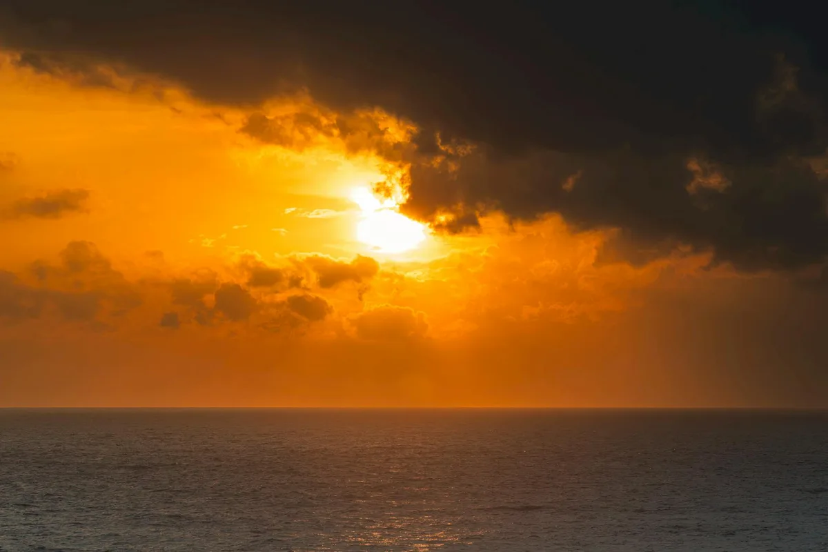 Oceano sereno al tramonto con nuvole drammatiche e tonalità dorate