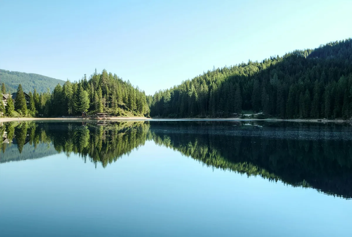 Vista serena di un lago di montagna con riflessi della foresta e cielo azzurro