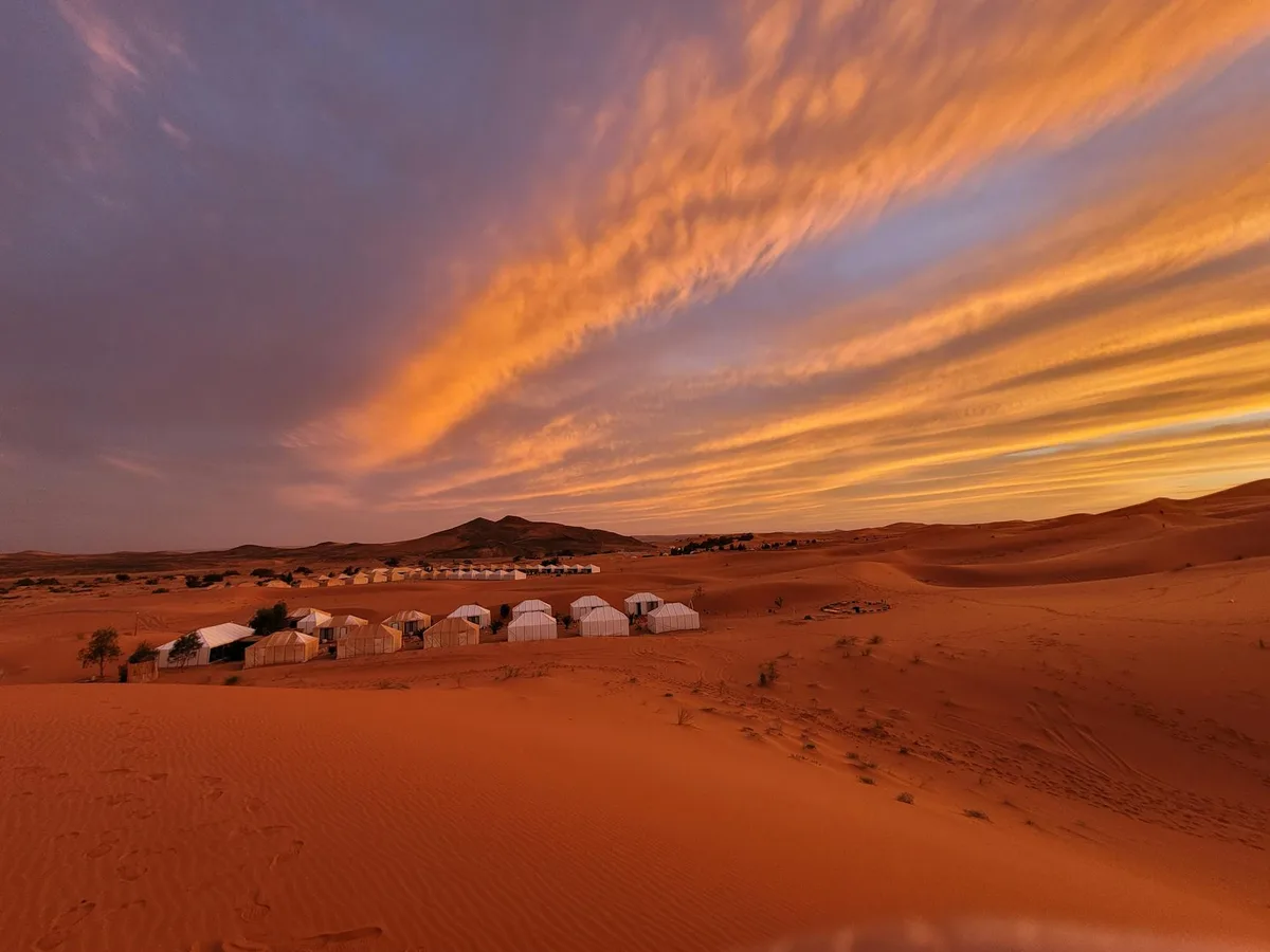 Tentes blanches dans le Sahara sous un coucher de soleil orange et bleu
