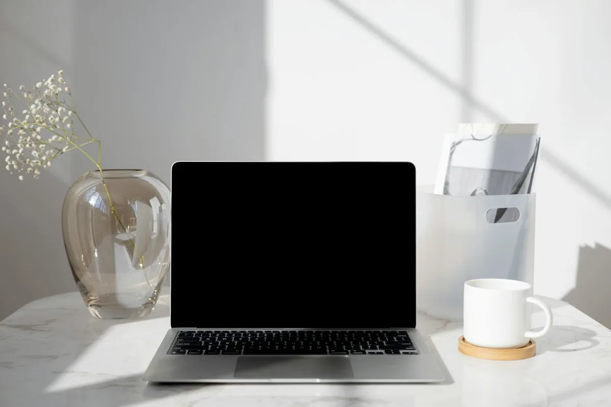 Mesa com laptop, café, vaso e documentos sob luz natural