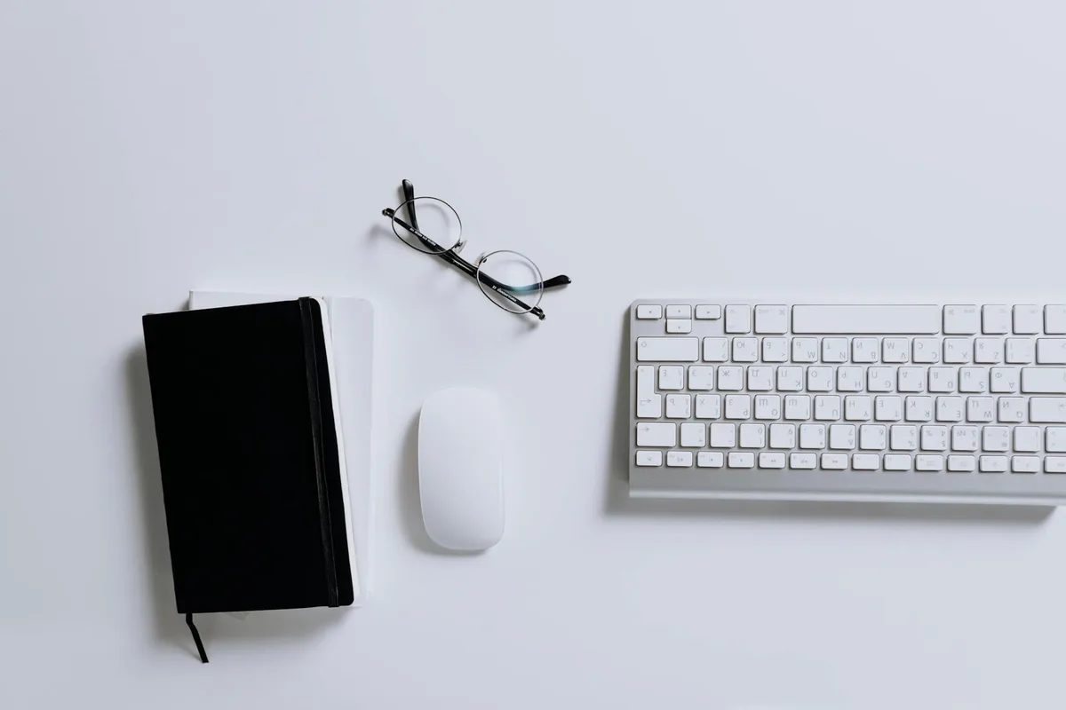 Spazio di lavoro moderno con tastiera, mouse, taccuino e occhiali su scrivania bianca