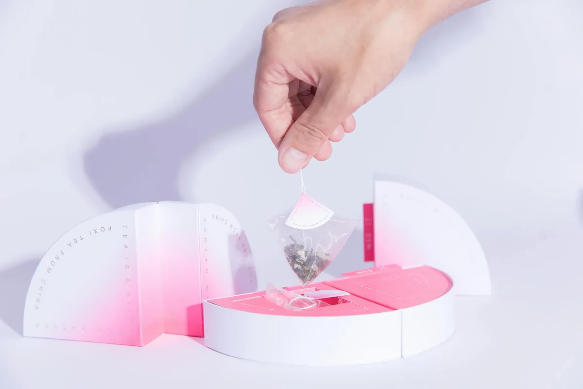 Hand hält Designer-Teebeutel über stilvoller Verpackung für moderne Teepräsentation