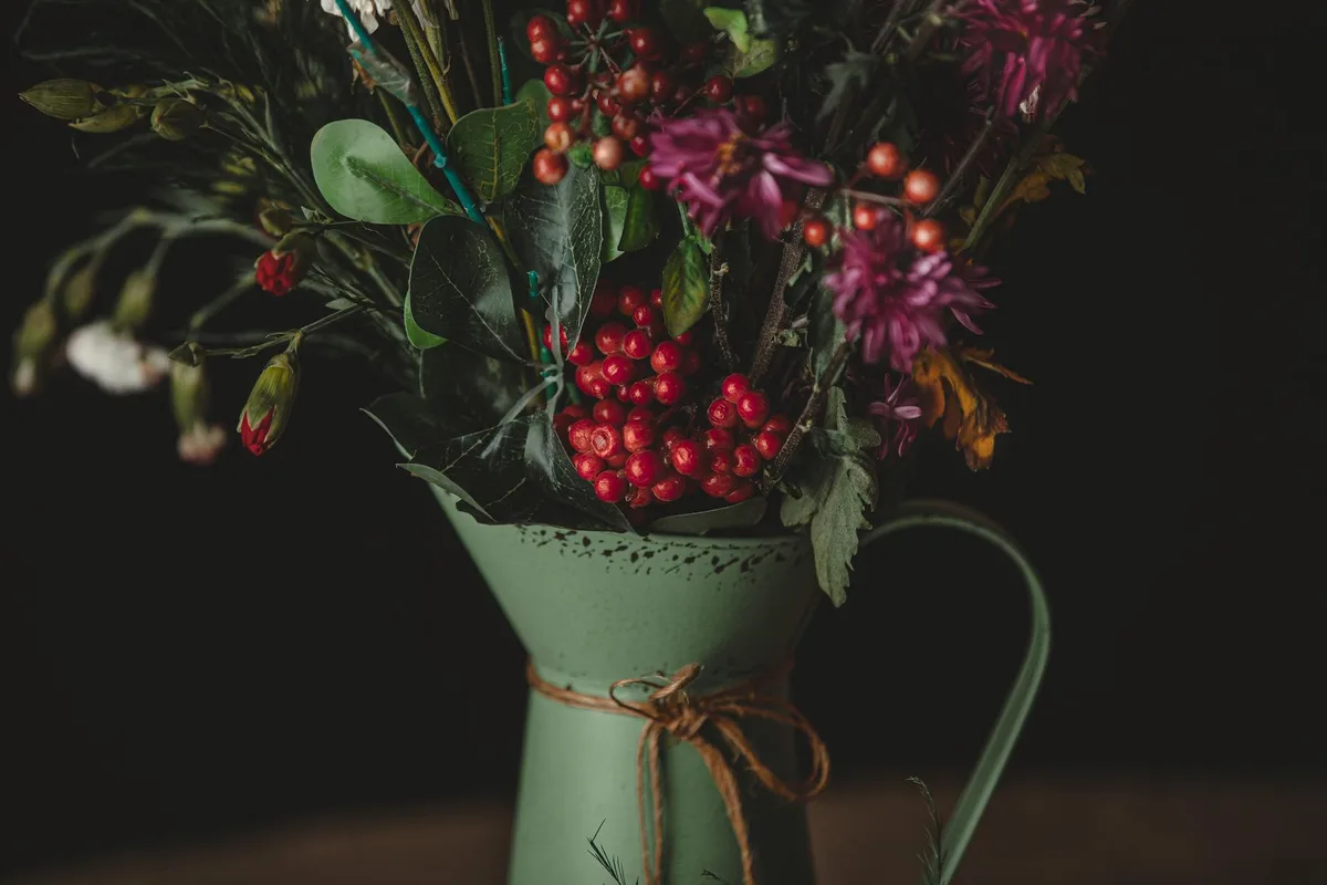 Rustikaler Blumenstrauß mit roten Beeren im Vintage-Krug.