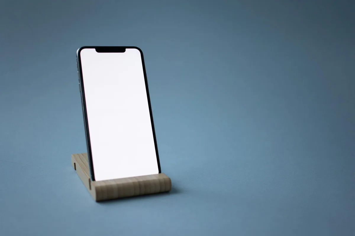 Smartphone elegante su supporto di legno minimalista su sfondo neutro, perfetto per display tech.