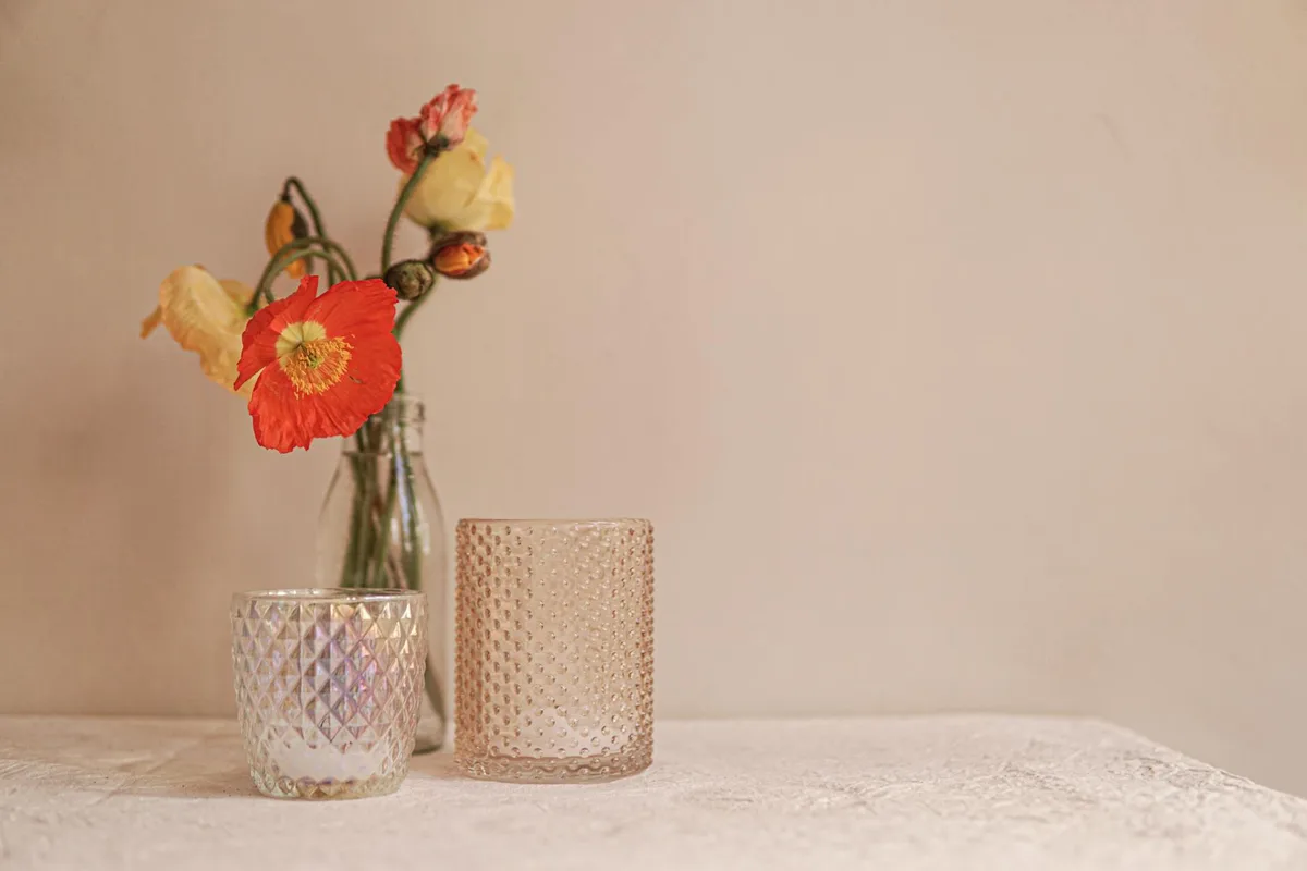 Vase en verre, coquelicots et verre texturé sur table neutre