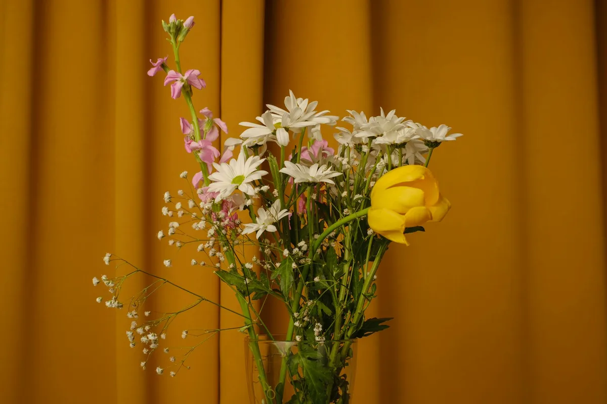 Яркий натюрморт с букетом в стеклянной вазе на фоне тёплой жёлтой шторы