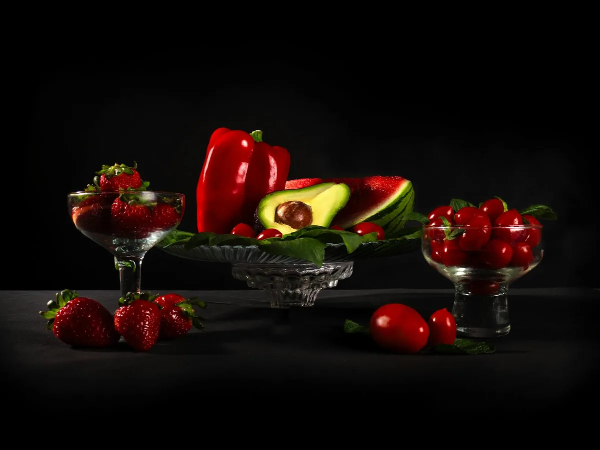 Lebendiges Stillleben mit frischen Erdbeeren, Tomaten, Avocado und roten Paprika auf dunklem Hintergrund
