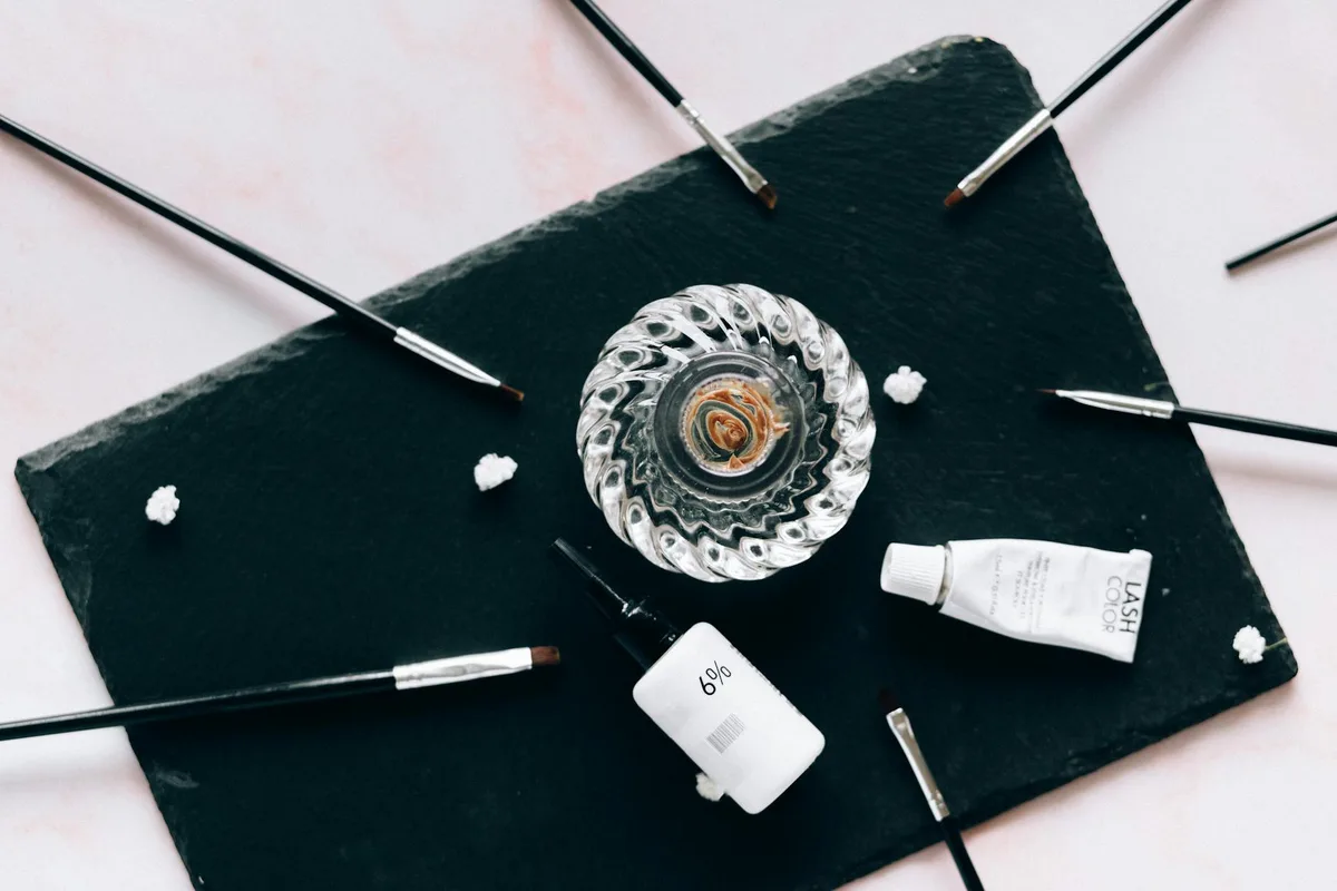 Disposizione estetica di cosmetici e pennelli su superficie di ardesia scura, perfetta per temi di bellezza e stile.