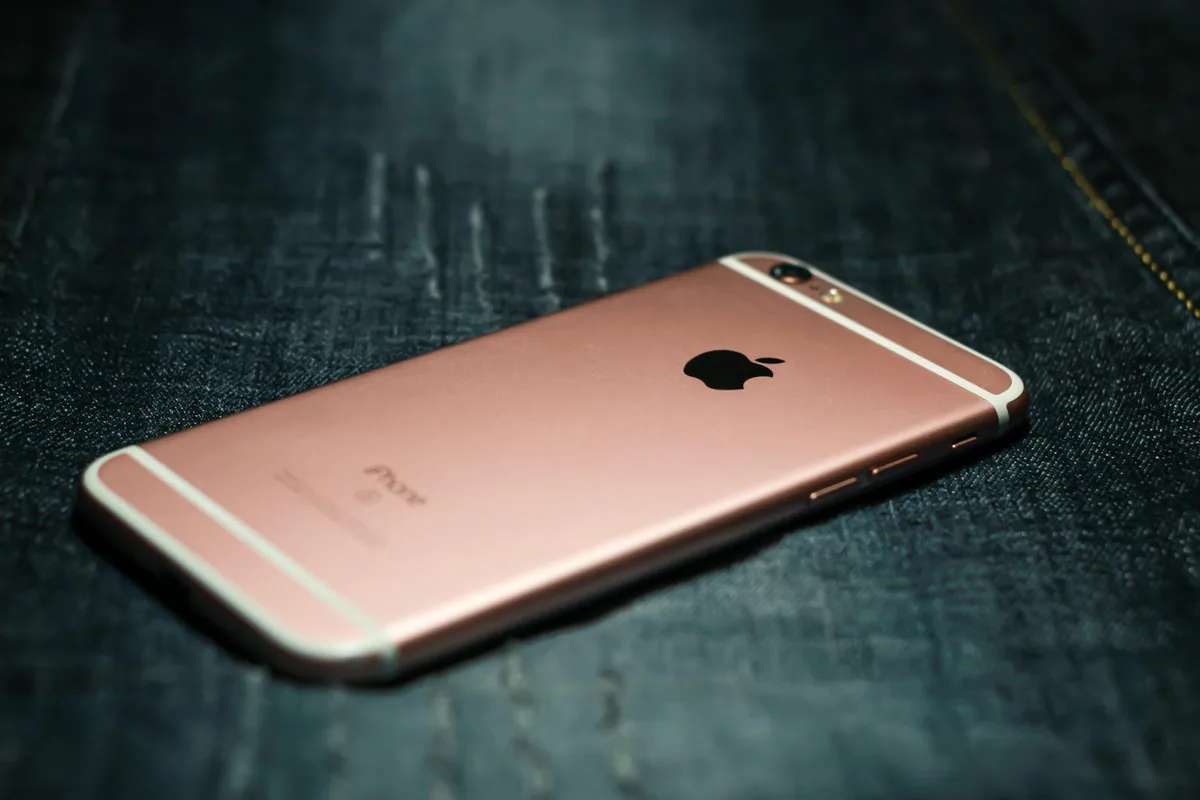 Smartphone oro rosa su denim scuro. Stile tech elegante.