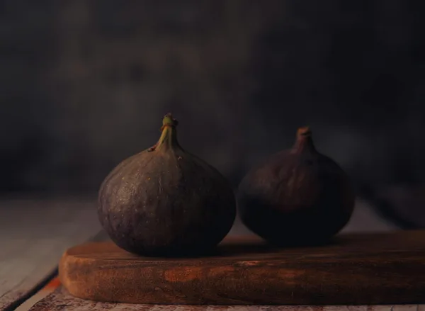 Close-up of two fresh figs resting on a rustic wooden board with a dark moody background.