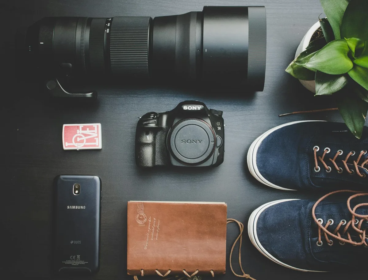 Flat lay creativo di attrezzatura fotografica, smartphone, quaderno, scarpe e pianta su legno