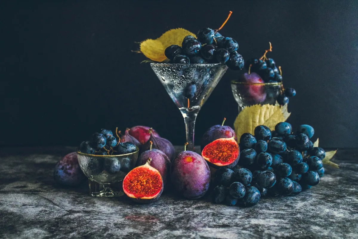 Natura morta scura di uva fresca e fichi in vetro, sapori autunnali