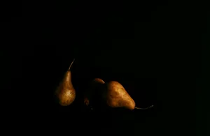 Dramatic still life of ripe pears in low lighting against a black background.