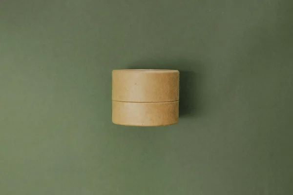 エコ段ボールの化粧品容器をミニマルなグリーン背景で表現。サステナブルビューティのコンセプト。