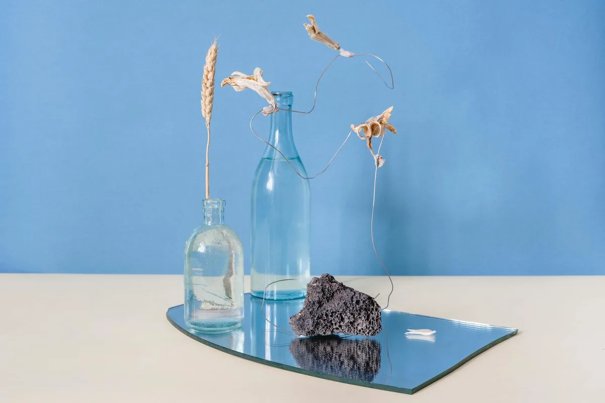 Composizione elegante di erbe secche e bottiglie su specchio con sfondo blu.