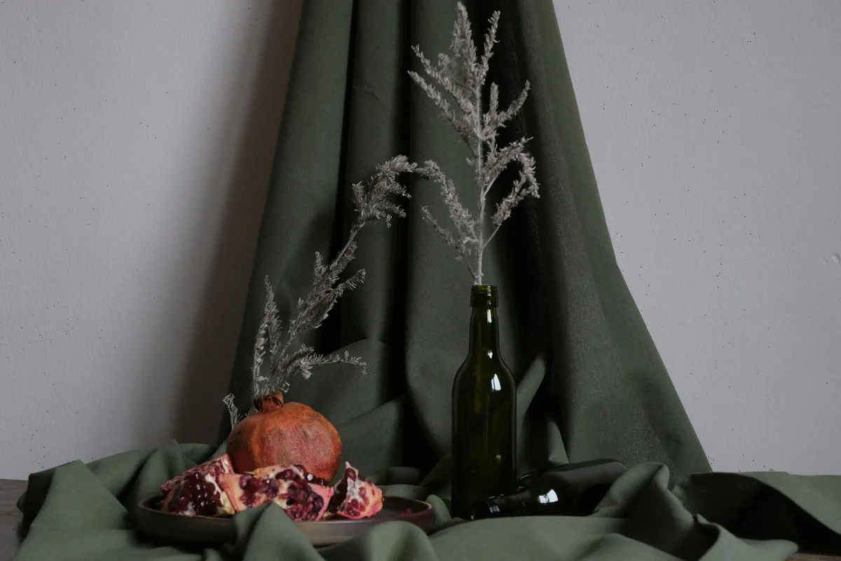 Elegant still life featuring pomegranate and branches on green fabric backdrop.