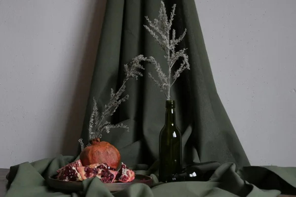 Elegant still life featuring pomegranate and branches on green fabric backdrop.