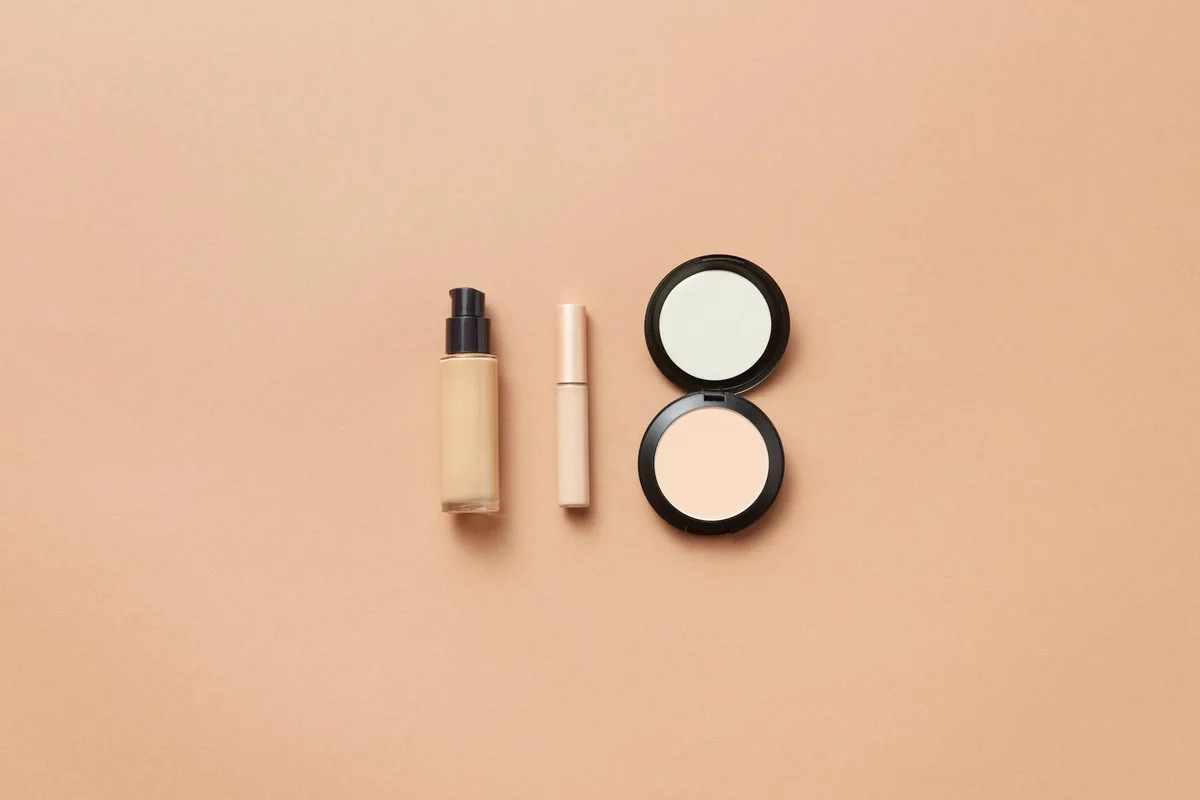 Flatlay von Foundation, Concealer und Kompaktpuder auf beigem Hintergrund für Beauty-Themen