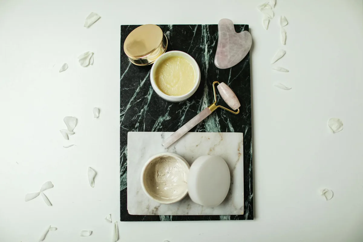 Flatlay: strumenti skincare e creme su marmo con petali.