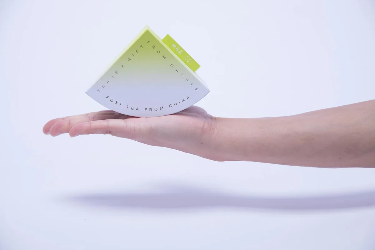 Hand hält Tee-Paket mit Verlauf und Text auf weißem Hintergrund