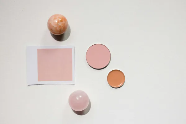 Flat lay minimalista con prodotti makeup e sfere di marmo su superficie bianca