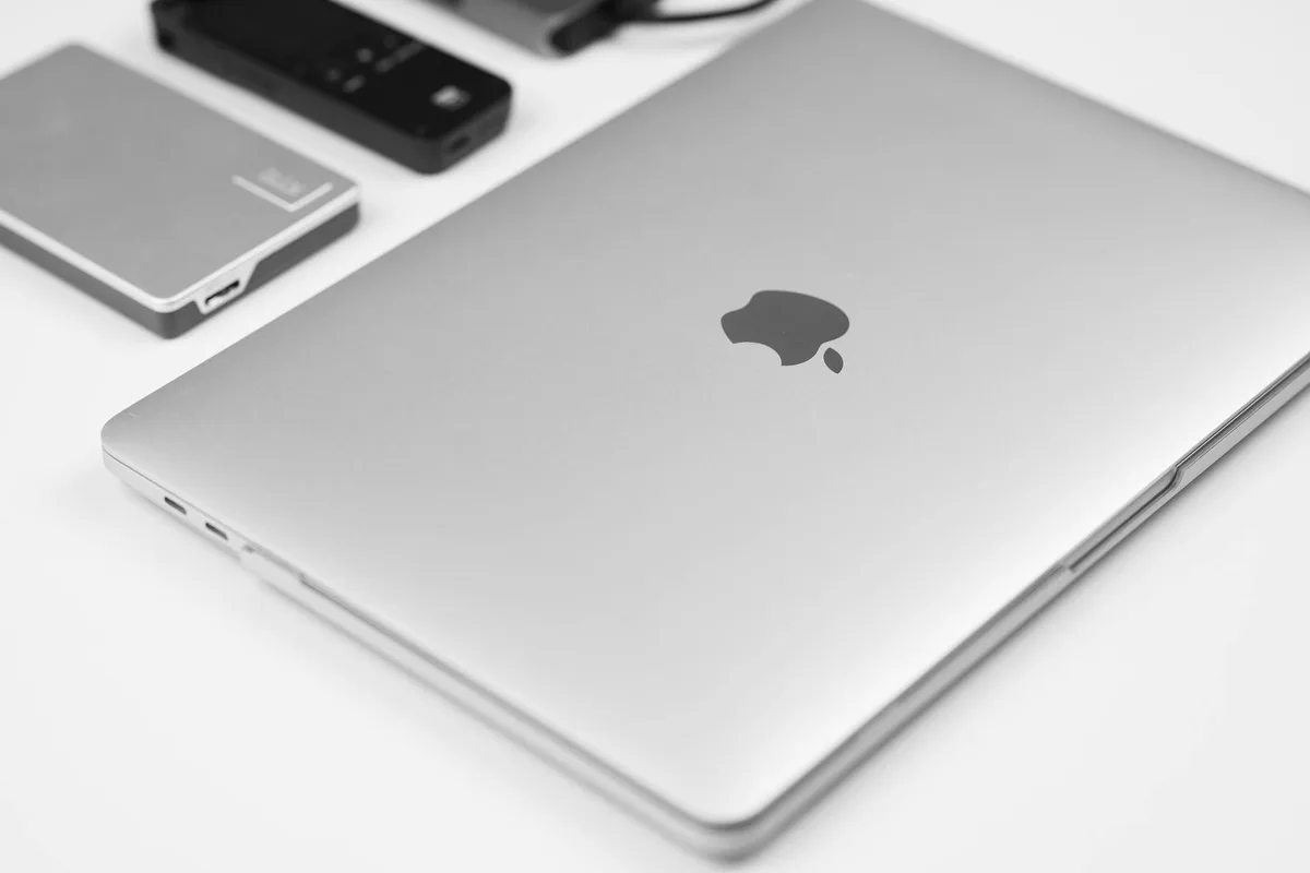 Minimalistisches Flatlay eines silbernen Laptops mit Tech-Zubehör auf weißem Untergrund