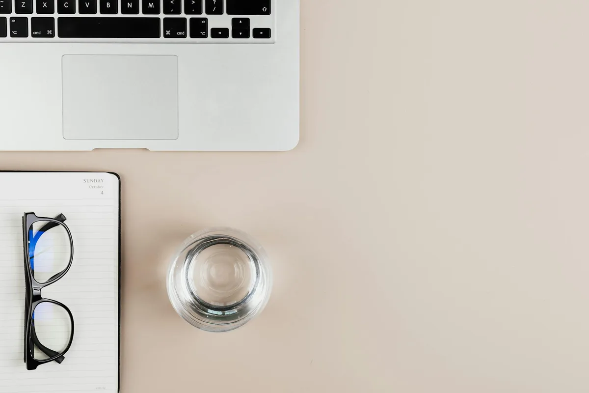 Vista dall'alto di scrivania ordinata con laptop, taccuino, occhiali e acqua