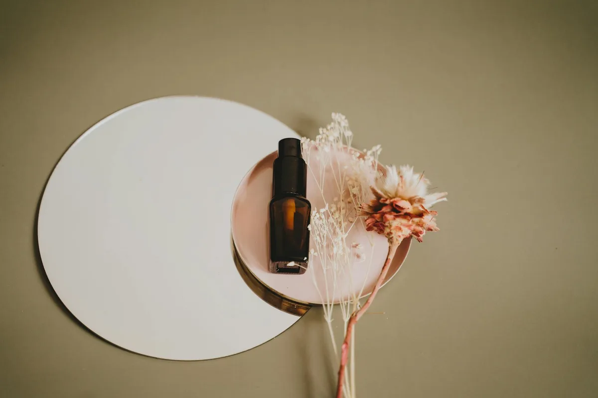 Stilvolle Kosmetikpumpe auf Spiegel und rosa Teller mit zarten Trockenblumen