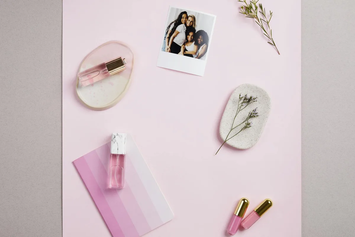Elegante flat lay con profumi rosa, decor floreali e foto casual su sfondo rosa pastello