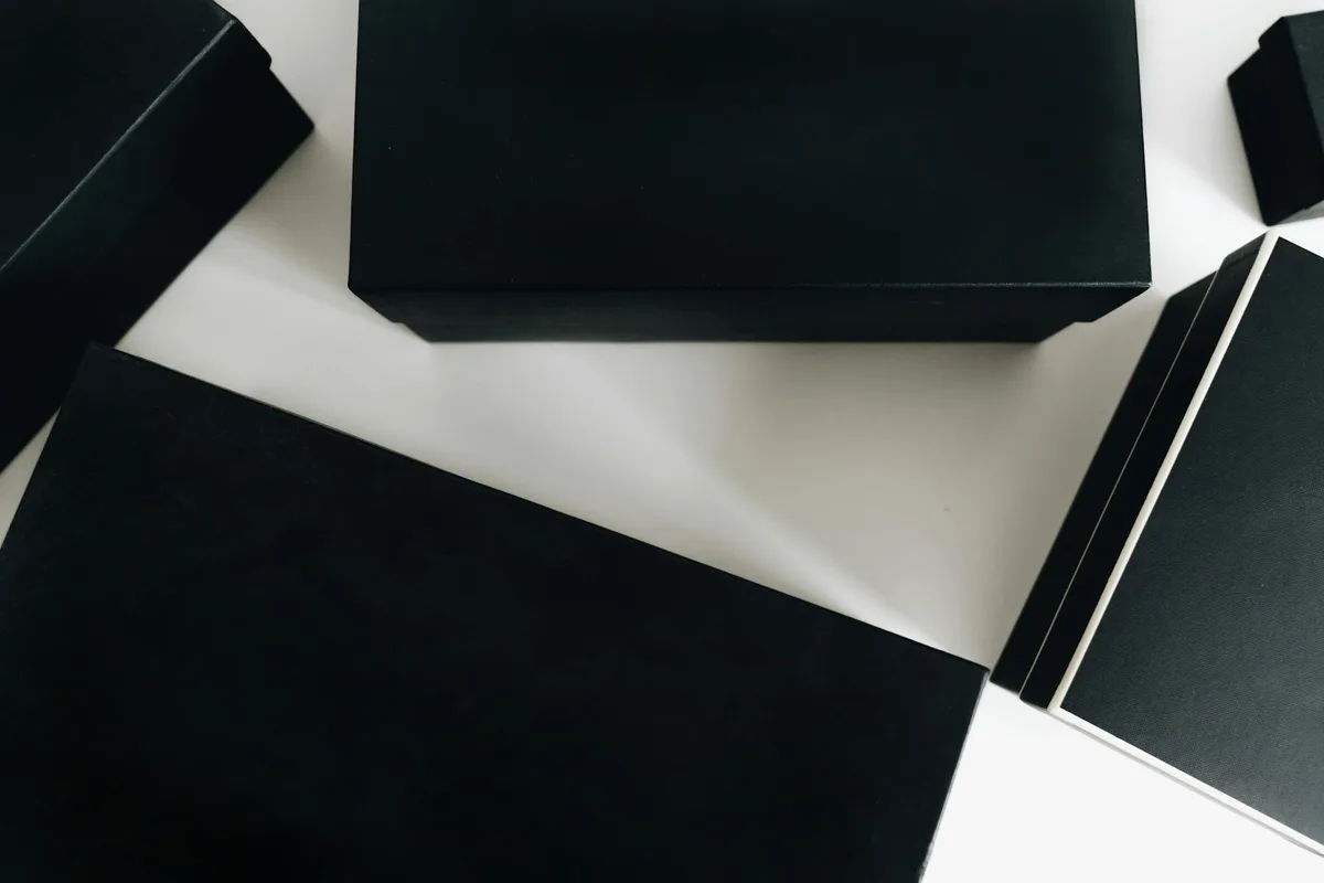 Vista dall'alto di eleganti scatole nere disposte artisticamente su superficie bianca, design minimalista.