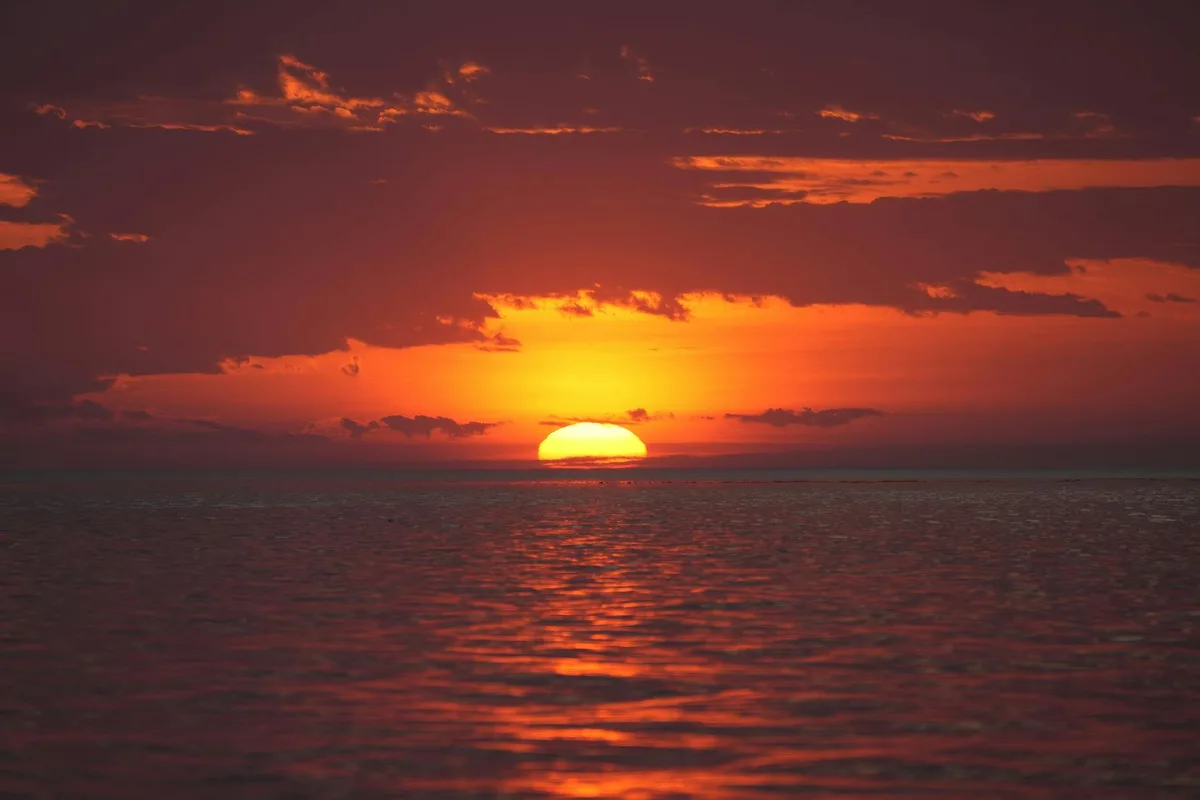 Tramonto sull'oceano con riflessi rossi e arancioni vividi sull'acqua