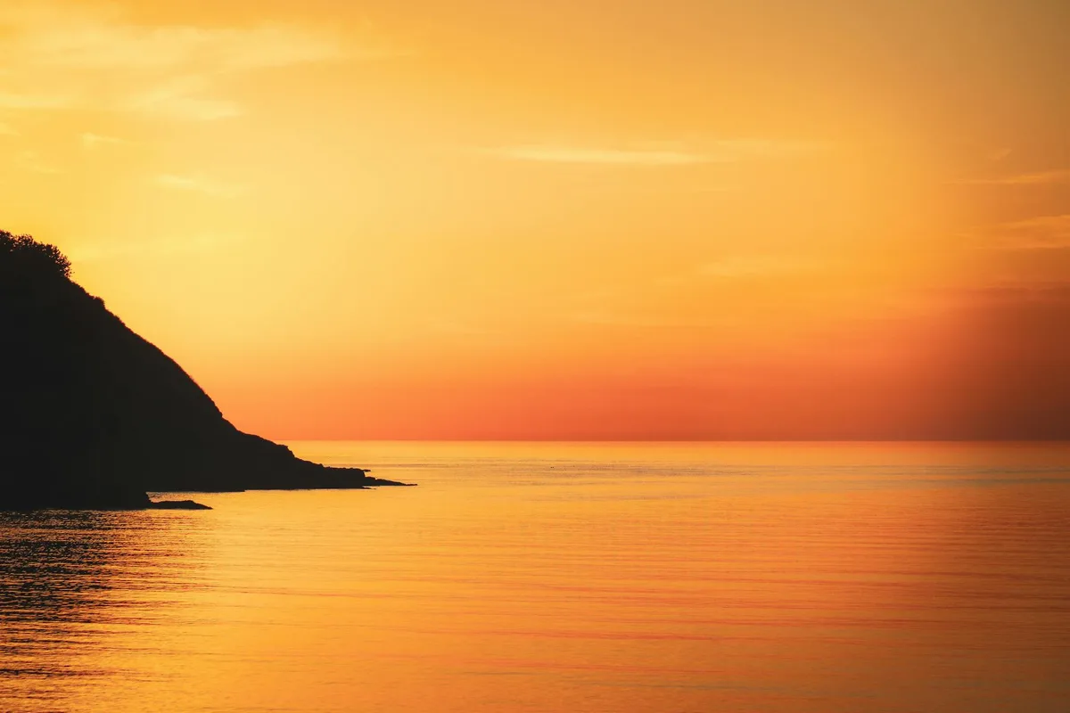 Tramonto vibrante sull'oceano con sagoma di scogliera