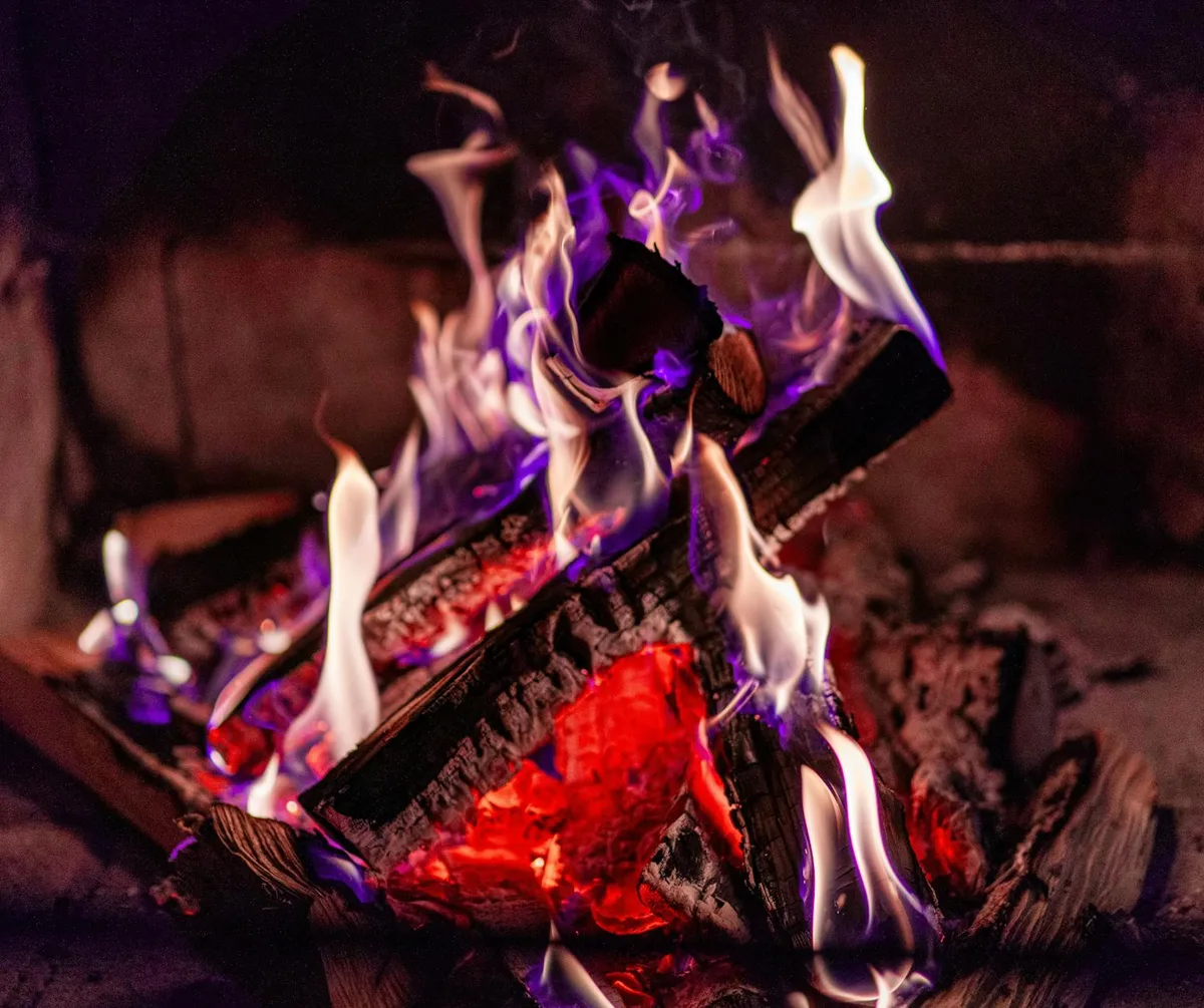 A close-up image of a cozy fireplace with burning firewood and bright glowing flames.