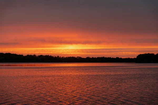 Faszinierender Sonnenuntergang über einem ruhigen See mit lebendigen Orangetönen, die auf dem Wasser reflektieren