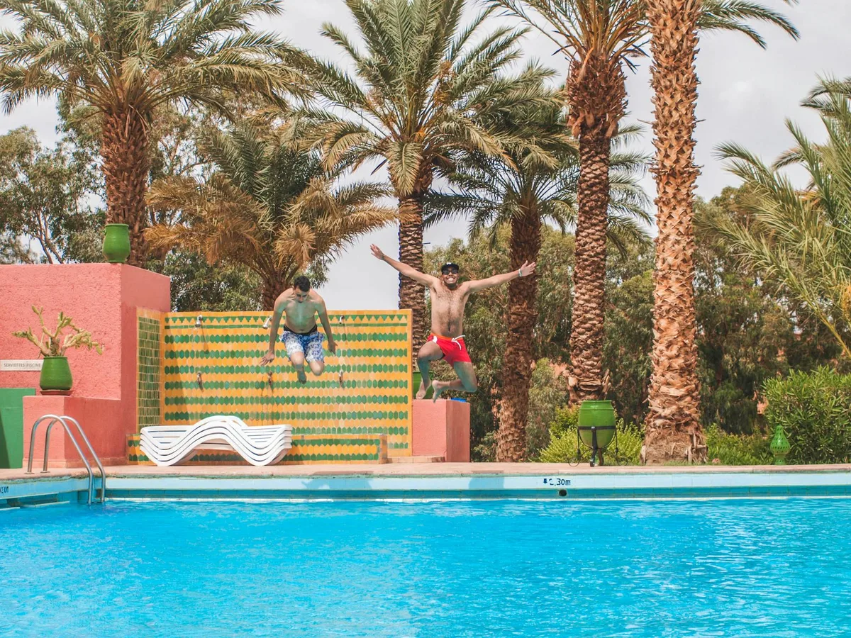 Due uomini saltano gioiosi in piscina tra palme tropicali