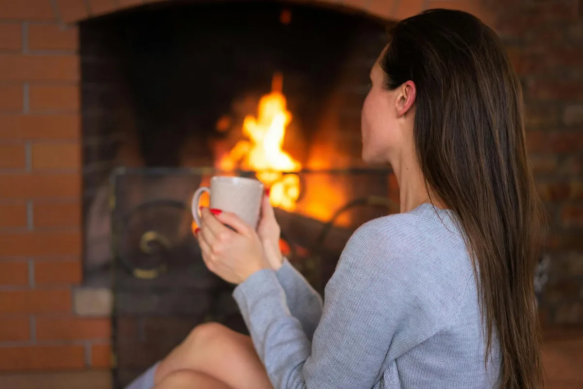 Женщина наслаждается горячим напитком у камина, создавая уютную атмосферу