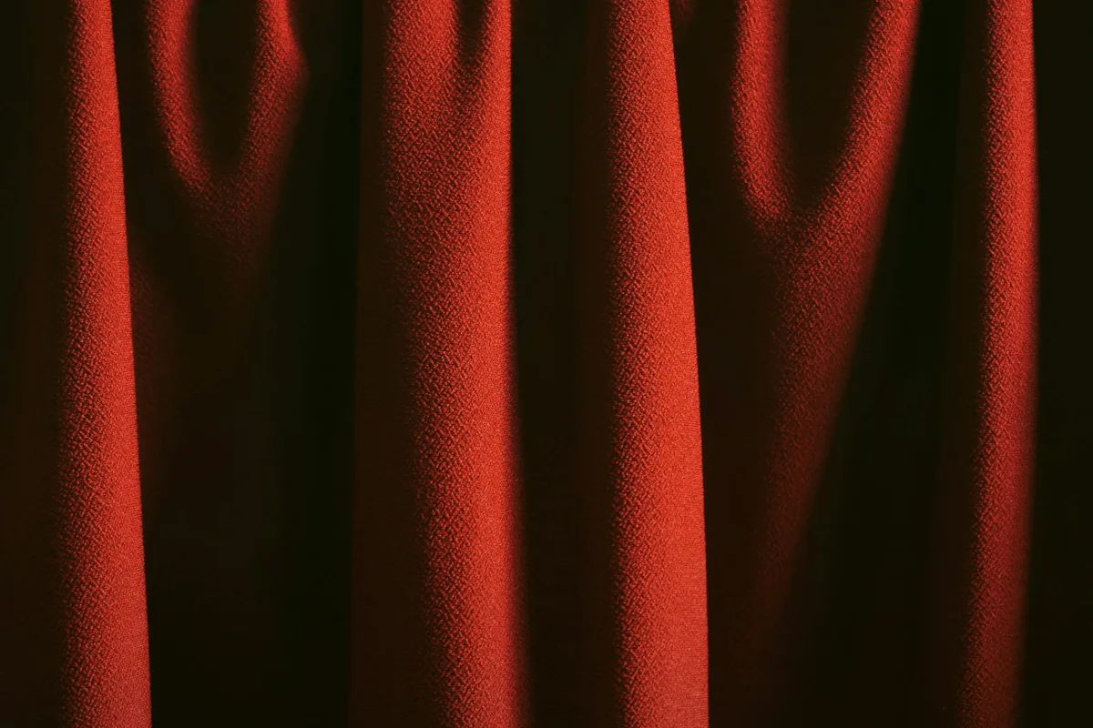 Classica tenda rossa con texture ricca e pieghe eleganti in luce soffusa.