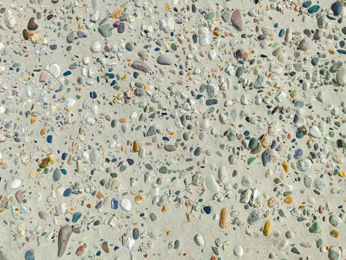 Bunte Kieselsteine detailliert auf einer sandigen Strandoberfläche verstreut.