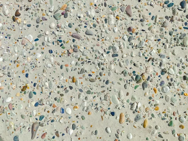 Ciottoli colorati sparsi su una superficie di sabbia in dettaglio.
