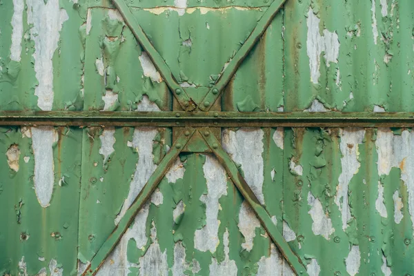 Close-up of a green rusty metal gate showing peeling paint and weathered texture.