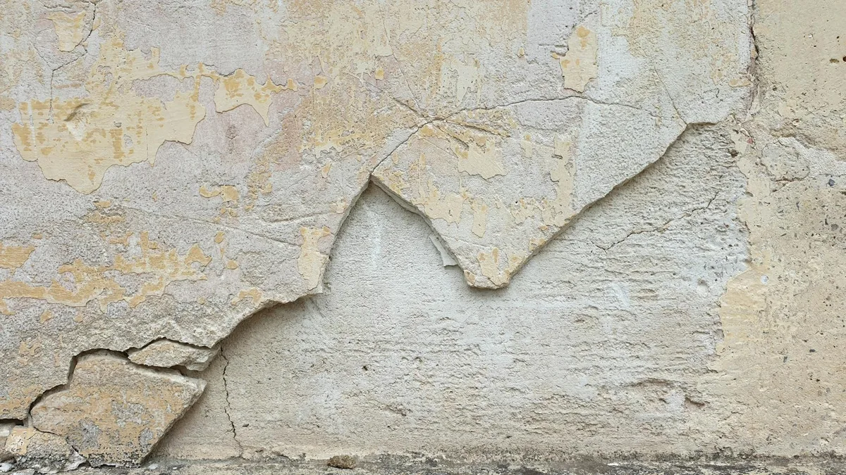 Detailansicht einer rissigen, abblätternden beigen Betonwandtextur