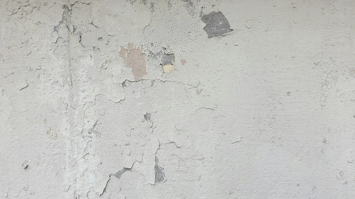 Vista dettagliata muro cemento con vernice scrostata e crepe, texture sfondo