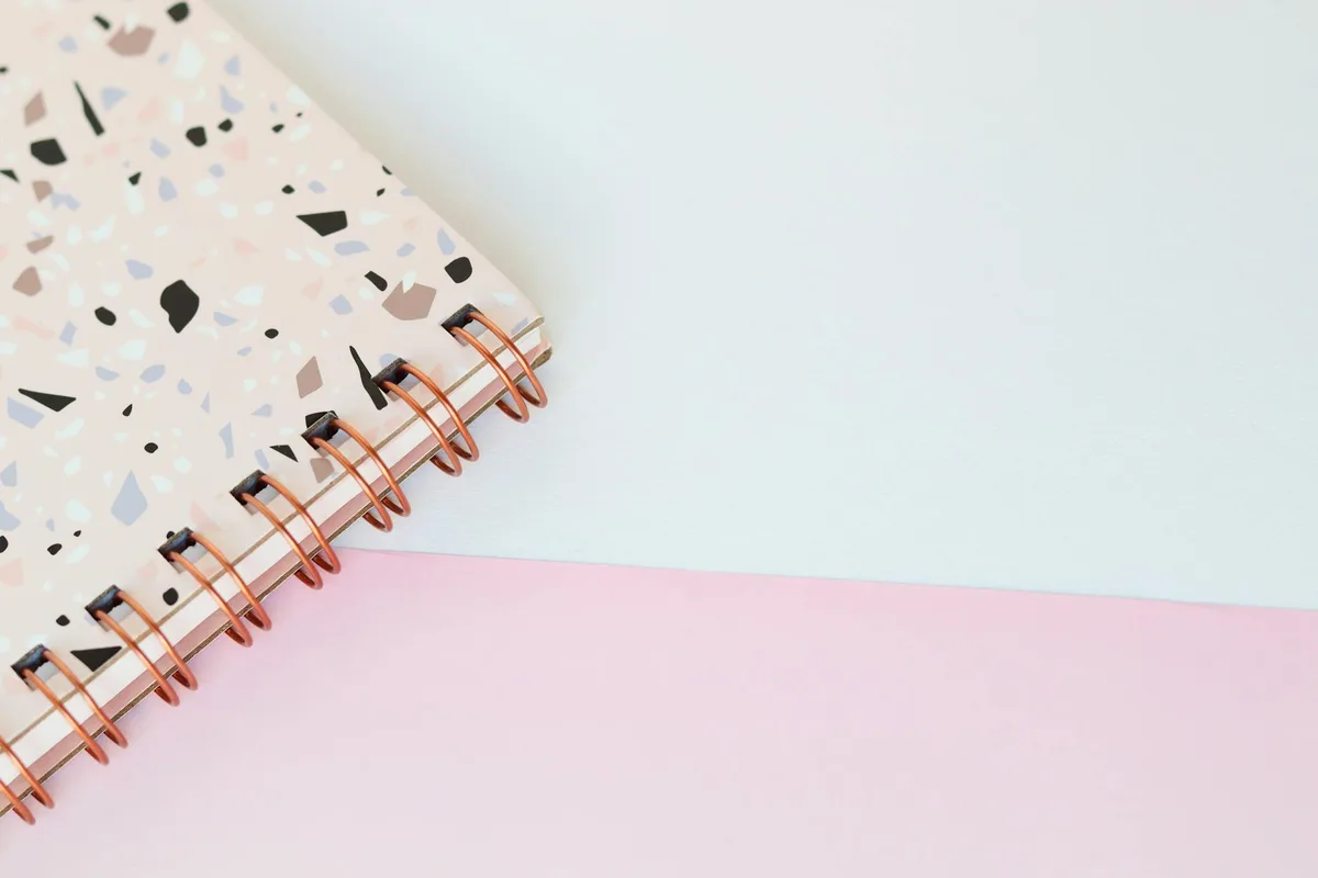 Elegantes rosa-weißes Terrazzo-Notizbuch mit Spiralbindung auf pastellfarbenem Schreibtisch