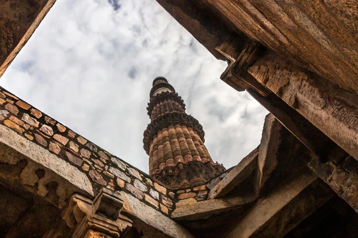 Vista dal basso del Qutub Minar a Delhi con mura di pietra e cielo nuvoloso