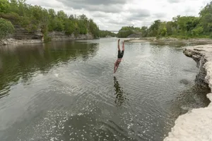 A man gracefully dives into a tranquil river surrounded by rocky formations and greenery.