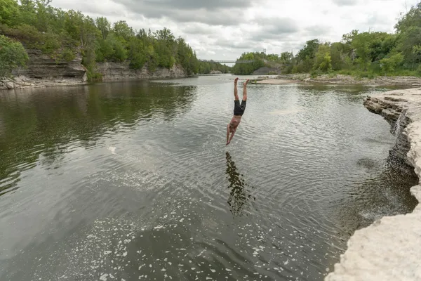 A man gracefully dives into a tranquil river surrounded by rocky formations and greenery.